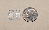 Lentes intraocular junto a una moneda de 10 centavos para comparar el tamaño.